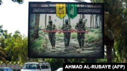 IRAQ -- A picture taken on June 20, 2018 shows a propaganda billboard for the pro-Iran Hezbollah Brigades militia hanging over Palestine Street in the centre of the Iraqi capital Baghdad, depicting three of their masked fighters walking along a road betwe