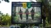 IRAQ -- A picture taken on June 20, 2018 shows a propaganda billboard for the pro-Iran Hezbollah Brigades militia hanging over Palestine Street in the centre of the Iraqi capital Baghdad, depicting three of their masked fighters walking along a road betwe