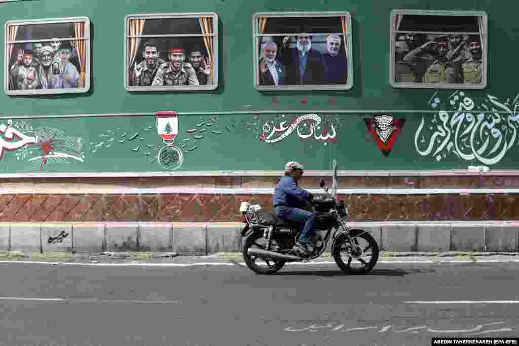 An Iranian rides a motorbike past billboards on Enqelab Square in Tehran.