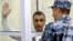 Un gardian încătușându-l pe Lev Șlosberg la un tribunal din Pskov, pe 17 august 2026.