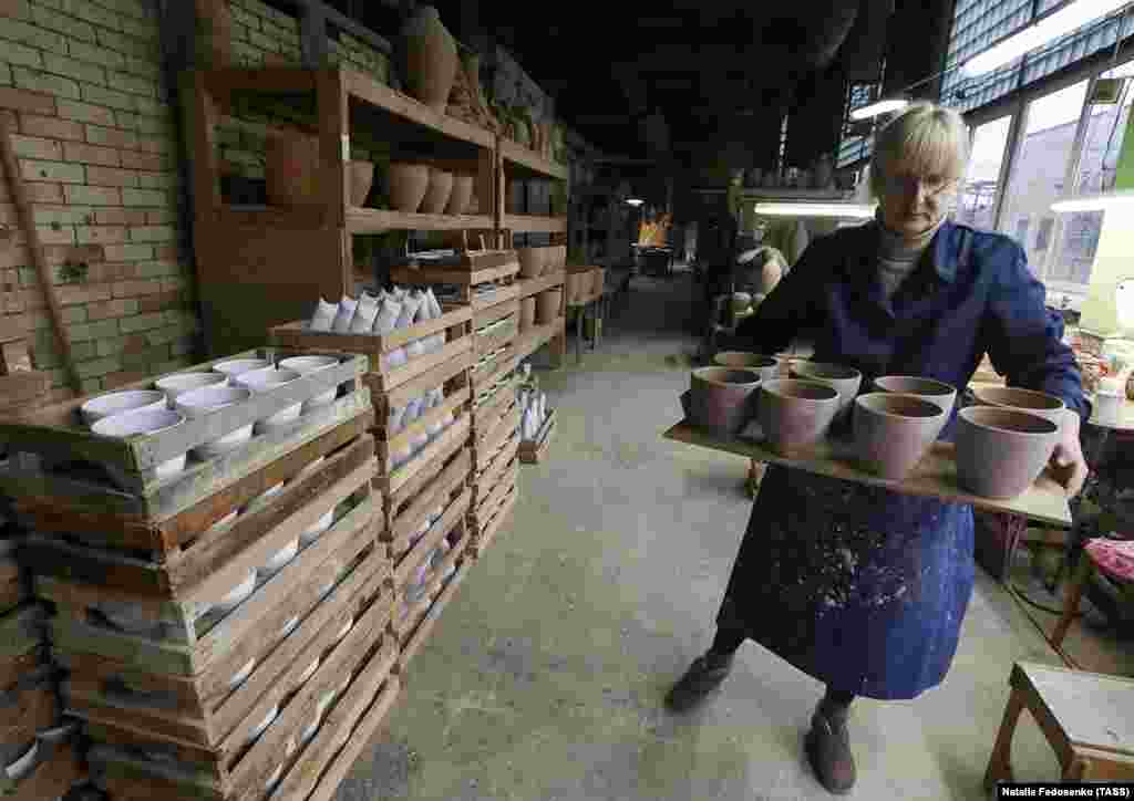 A worker carries clay pots that await firing in a kiln and a painter&rsquo;s touch.