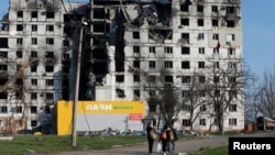 Local residents walk past a destroyed apartment building in Mariupol on April 20. 