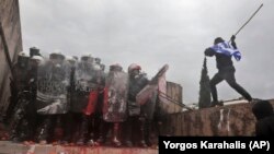 A demonstrator draped in the Greek flag attacks riot police with a stick during a rally against the agreement in Athens on January 20.