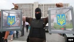 A masked pro-Russian separatist carries two ballot boxes from a seized polling station in Donetsk, Ukraine.