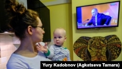 Ілюстраційне фото. Жінка тримає свого сина та дивиться телевізійну трансляцію щорічної прес-конференції російського президента Володимира Путіна в Москві, 14 грудня 2017 року
