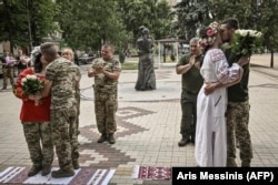 Ushtarët ukrainas martohen pranë monumentit të të dashuruarve (në sfond) gjatë një ceremonie martese në Druzhkivka në qershor 2022.