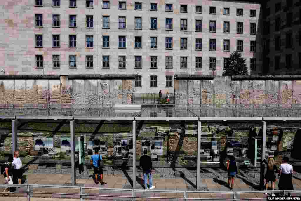 Disa vizitorë duke shikuar një ekspozitë pranë një pjese të mbetur të Murit të Berlinit, në vendin përkujtimor &quot;Topografia e terrorit&quot;, në Berlin. (12 gusht)