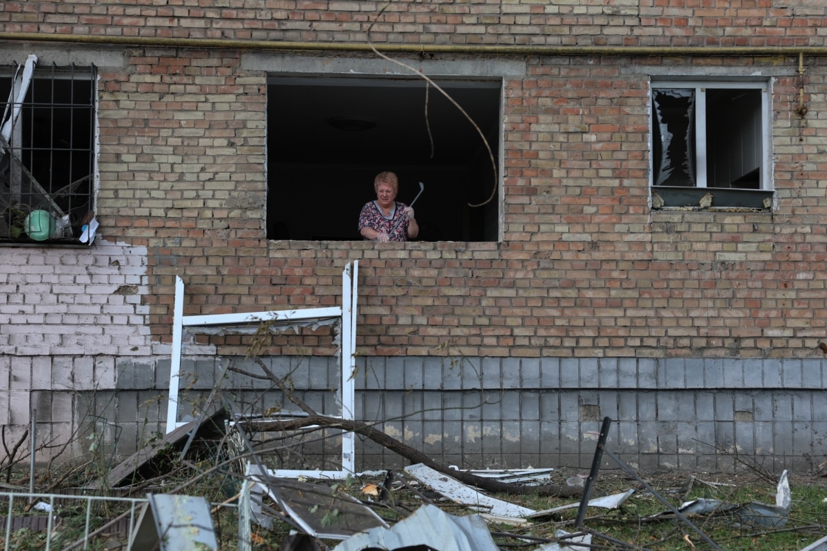 Жінка прибирає уламки скла на місці російської атаки