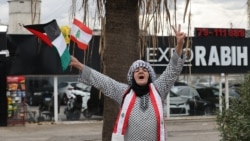 A woman waves the flags of Lebanon and Palestine as she greets people in the southern Lebanese city of Sidon on November 27, 2024, as displaced people make their way back to their homes in the south of Lebanon after a ceasefire between Israel and Hezbolla