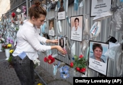 A volunteer dusts off portraits of St. Petersburg's medical workers who died from the coronavirus at an unofficial memorial in front of the local health department. The youngest worker honored there is 30-year-old nurse's aide Maria Tyshko.