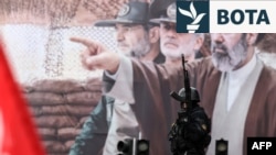 Një oficer i sigurisë iraniane qëndron roje pranë një billbordi me portretin e udhëheqësit të ri suprem të Iranit, Mojtaba Khamenei, në Teheran, më 13 mars.
