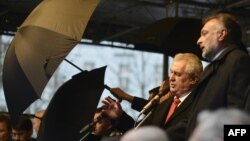 Ахоўнікі трымалі парасоны, калі людзі кідалі яйкі і памідоры ў прэзыдэнта Чэхіі Мілаша Зэмана 17 лістапада 2014 году. 