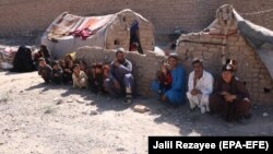 An internally displaced Afghan family sits outside a temporary shelter as they await relief from the authorities on the outskirts of Herat.