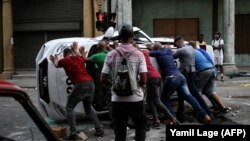Манифестанты в одном из районов Гаваны переворачивают и разбивают полицейскую автомашину, 11 июля 2021 года