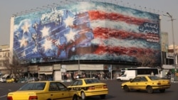 Тегерандағы Енгелаб алаңына ілінген баннерде Иран зымырандары АҚШ ұшақ тасығышын жойып жатқаны бейнеленген. Баннерде АҚШ үкіметіне қарата "Жел тұрғызамын деп құйында қалма" (If you sow the wind you will reap the whirlwind) деп жазылып тұр. 26 қаңтар 2026 жыл.