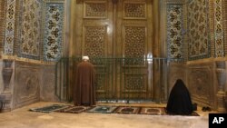 A cleric and a woman pray behind the closed door of Masoume Shrine in the city of Qom, some 80 miles (125 kilometers) south of the capital Tehran, Iran. March 16, 2020