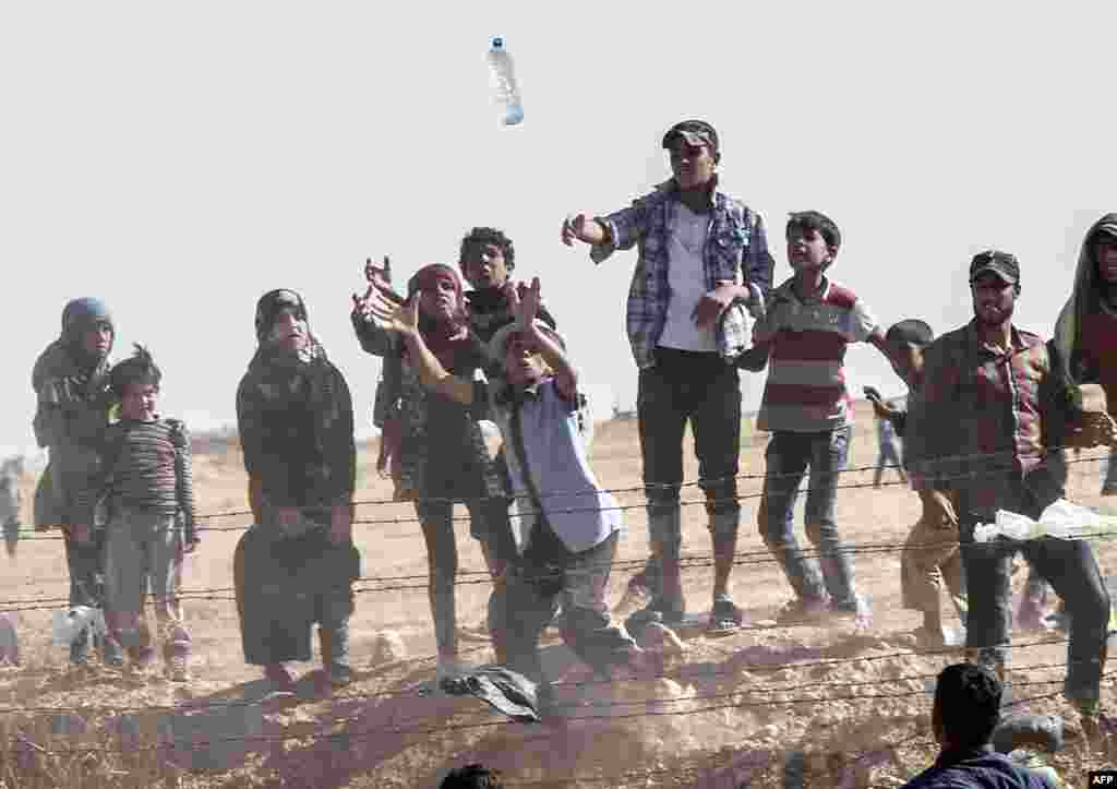 Syrian refugees try to grab bottles of water thrown from the Turkish side of the border near the Syrian town of Tal Abyad, at Akcakale in Sanliurfa Province. (AFP/Bulent Kilic)