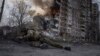 Украински полицай се прикрива пред горяща сграда, пострадала при руски въздушен удар в Авдиивка през март 2023 г