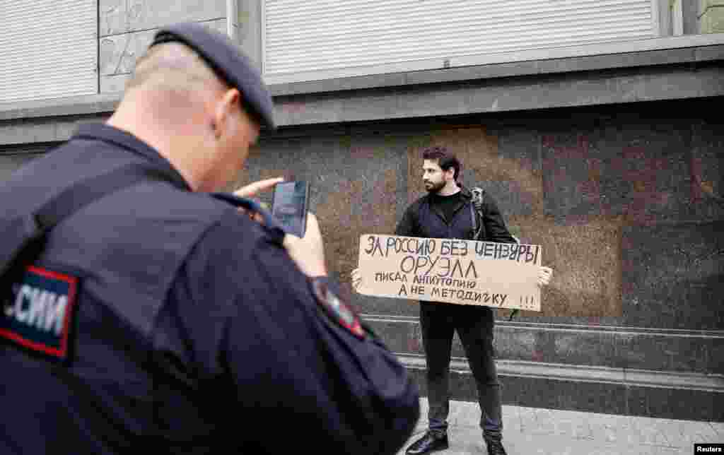 Policajac fotografira političkog stratega Dmitrija Kisijeva koji prosvjeduje zbog izmjena zakona kojim bi se trebala uvesti ograničenja u pretraživanju interneta, Moskva, Rusija, 22. srpnja 2025. Poruka na transparentu glasi: "Za Rusiju bez cenzure. Orwell je napisao distopiju, a ne priručnik za obuku".