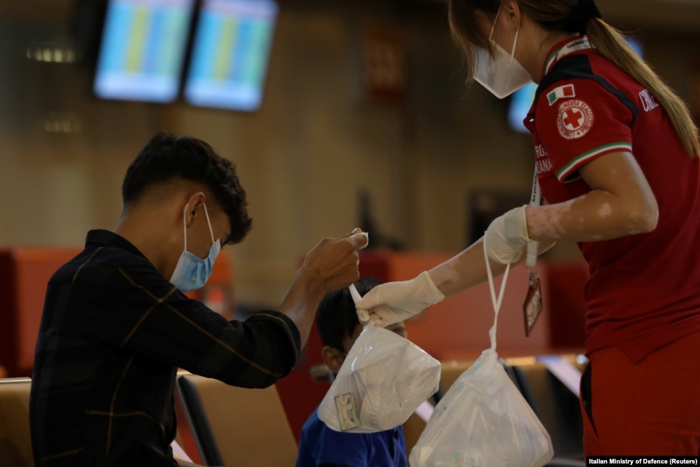 Një djalë afgan merr një qese me ushqim nga një punëtore e Kryqit të Kuq, pasi ai arrin më 16 gusht në aeroportin Fiumicino të Romës.