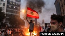 Протестиращ развява ливанското знаме по време на шествие по повод годишнината от експлозията на пристанището в Бейрут. Шествието прерасна в сблъсъци между демонстрантите и силите за сигурност.