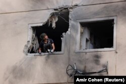 Egy izraeli rendőrségi utász néz ki egy Gázából kilőtt rakéta által megrongált ház ablakán a dél-izraeli Askelón városban, 2021. május 11-én