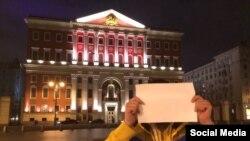 Журналист Филипп Киреев прикрывается бумажкой на фоне здания московской мэрии