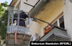 A woman speaks with a work crew amid the crackdown on unauthorized balcony reconstructions in Bishkek. The asbestos panels around the woman's balcony were removed soon after this picture was taken on June 26.