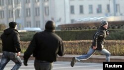 Belarusian plainclothes police chase a protester on Independence Square in Minsk after he pelted eggs at a statue of Lenin. 