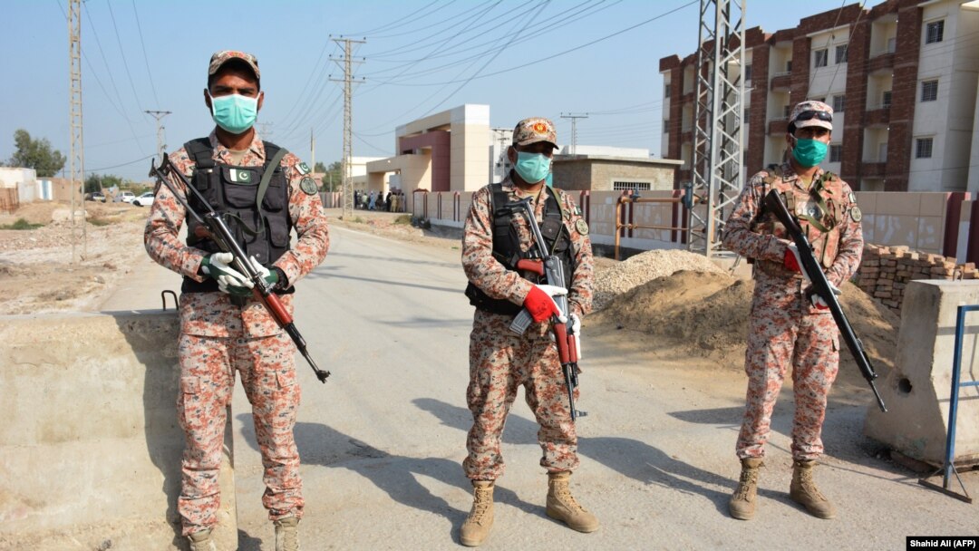 Soldiers wearing facemasks stand guard on road leading to a quarantine faciltity (R) for people returning from Iran via the Pakistan-Iran border town of Taftan to prevent the spread the coronavirus in Sukkur, a city in southern province of Sindh.