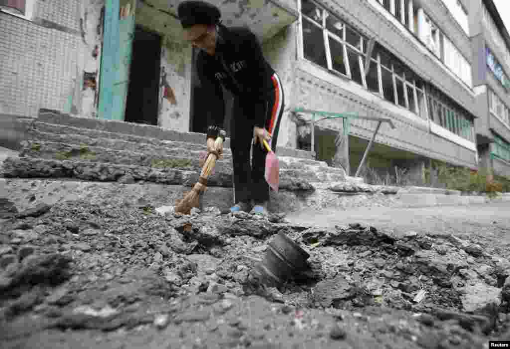 A resident clears debris next to a crater with the remains of a rocket shell in the eastern Ukrainian town of Debaltseve. (Reuters/David Mdzinarishvili) 