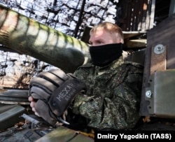A Russian tank crewman photographed beneath a hedgehog armor cage