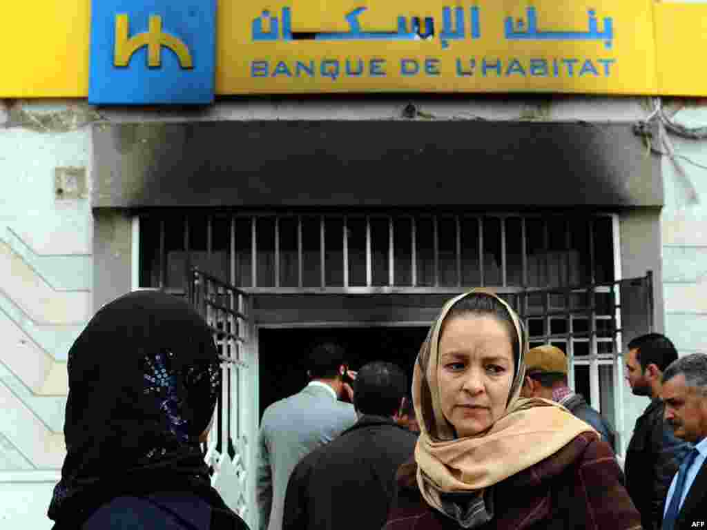 تجمع مردم بیرون از یک بانک در شهر تونس که در جریان اعتراضها به آتش کشیده شده است.