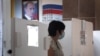 With a portrait of President Vladimir Putin in the background, a woman in Moscow prepares to cast her ballot during early voting in a controversial plebiscite on amendments to the Russian Constitution. 