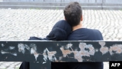 A young girl with a head scarf sits with a friend on a streetside bench in Brussels.