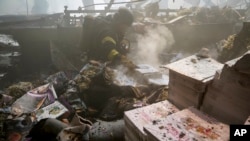 Pompierii se străduiesc să stingă un incendiu în timp ce un corp fără viață se află sub dărâmături după ce o rachetă rusească a lovit o mare tipografie din Harkov, Ucraina, la 23 mai 2024.