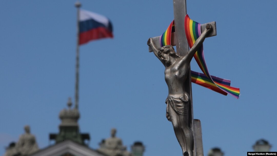 A rainbow ribbon tied to a crucifix is seen next to a Russian flag fluttering atop the State Hermitage Museum during an LGBT rally in St. Petersburg in August.