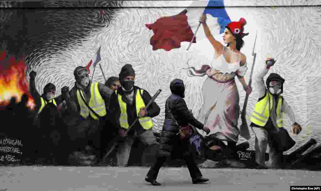 A woman in Paris passes by a mural inspired by the &quot;yellow-vest&quot; protesters. (AP/Christophe Ena)