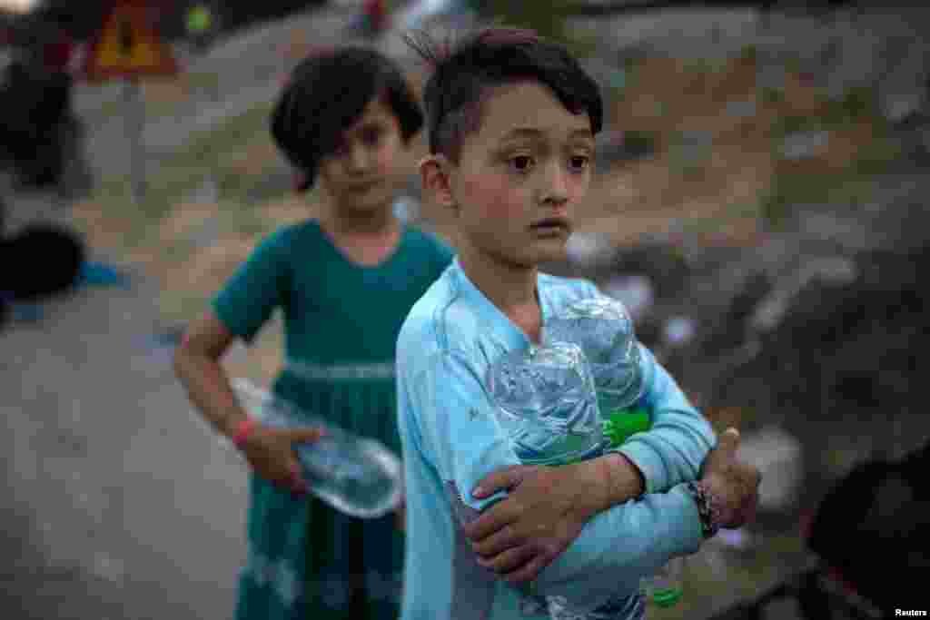 Një djalosh shihet duke mbajtur disa shishe me ujë teksa migrantët ikin nga kampi Moria.