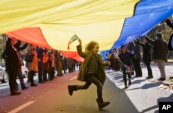 Un copil fuge pe sub un steag imens în timpul unui marș ce a avut loc în 2015, la București, cu ocazia celebrării a 94 de ani de la nașterea Regelui Mihai I.