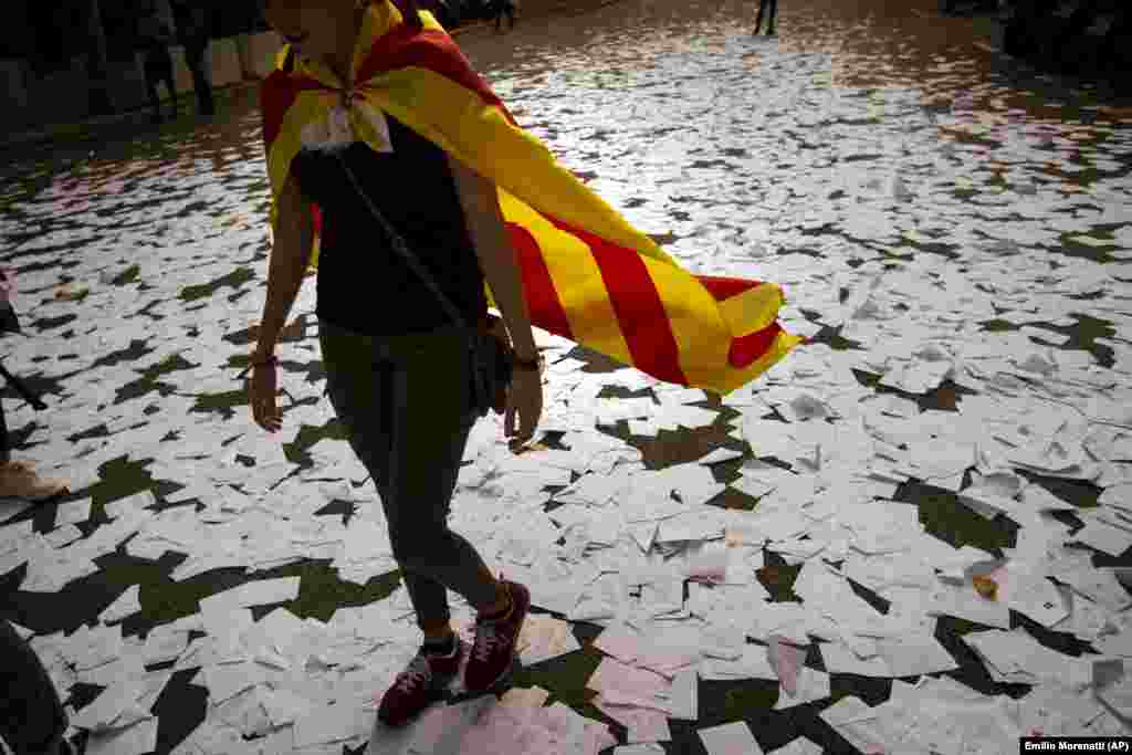 Жанчына з каталёнскім сьцягам ідзе па бюлетэнях, якія былі ўкінутыя прыхільнікамі незалежнасьці рэгіёну ад Гішпаніі. Барсэлона, 1 кастрычніка 2017.