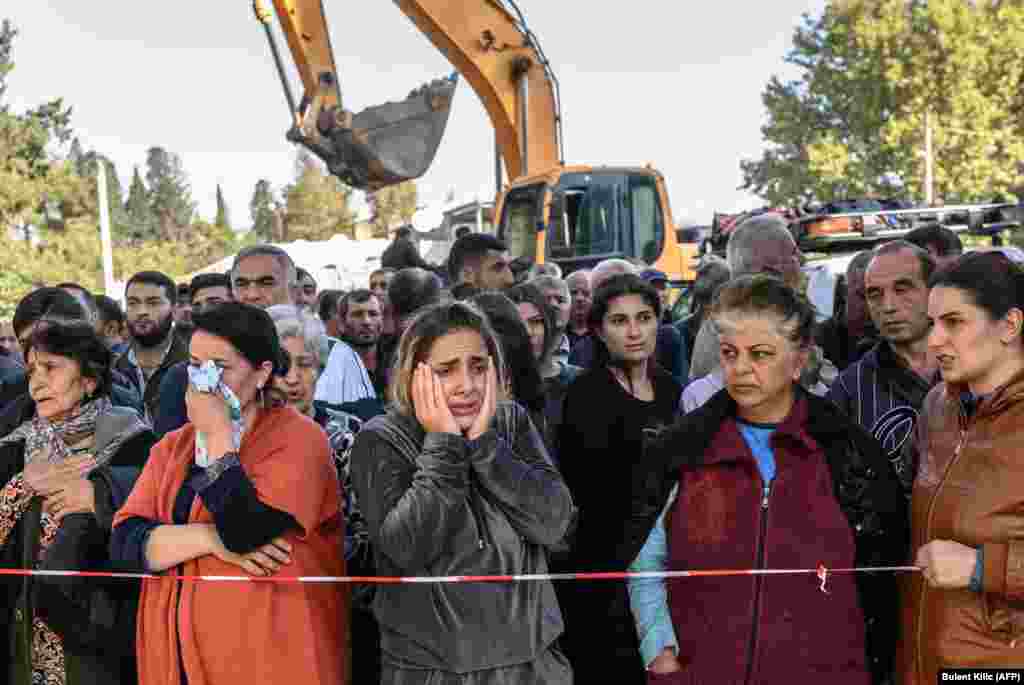 People stand behind caution tape as rescuers search for victims or survivors at a blast site hit by a rocket in the city of Ganca, Azerbaijan, during the fighting between Armenia and Azerbaijan over the breakaway region of Nagorno-Karabakh on October 11.