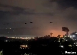 Хеликоптери в небето над Каракас, Венецуела, където се издига дим от експлозии, 3 януари 2026 г.