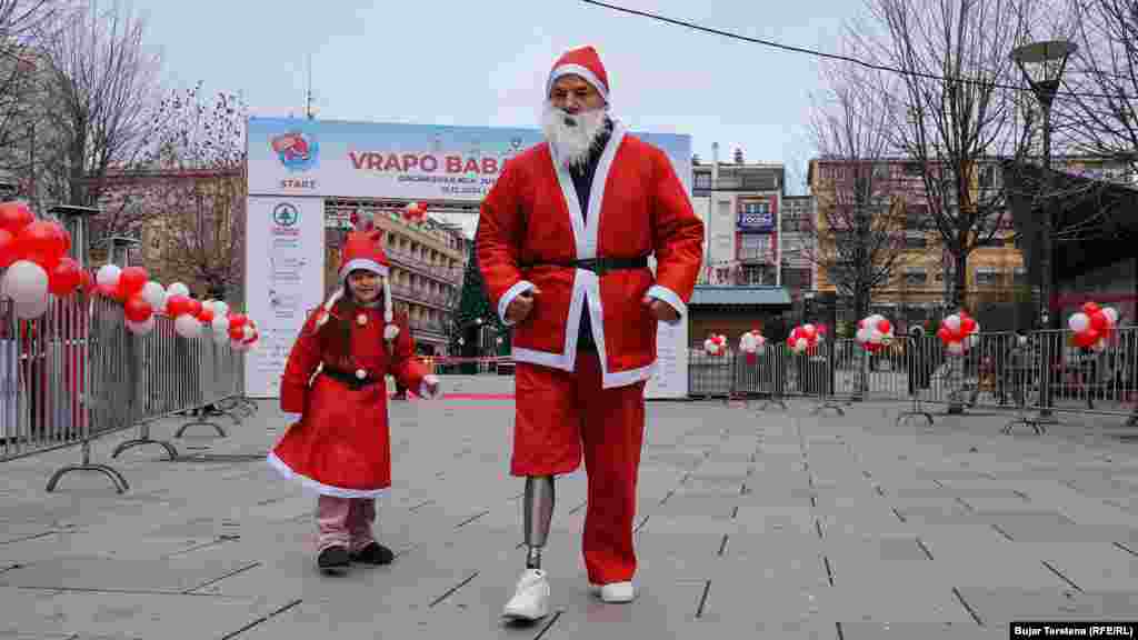 Një vajzë e vogël dhe një burrë &quot;me këmbë protetike të veshur me kostume të kuqe marrin pjesë në edicionin e nëntë të mini-maratonës &ldquo;Vrapo Babadimër&rdquo; në Prishtinë, që ka për qëllim mbledhjen e fondeve për çështje humanitare.