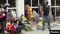 A woman places flowers as Interior Ministry troops stand guard outside a gun shop that was attacked during the funeral of salesman Andrei Maksimenko in Aqtobe on June 8.