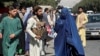 Forțele talibane blochează drumurile din jurul aeroportului, în timp ce o femeie îmbrăcată în Burqa trece pe lângă, Kabul, Afganistan. Fotografie realizată în 27 august 2021.