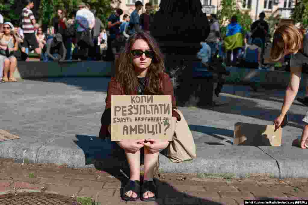 Дівчина прийшла на протест із запитанням на банері: «Коли результати будуть важливіші за амбіції?»