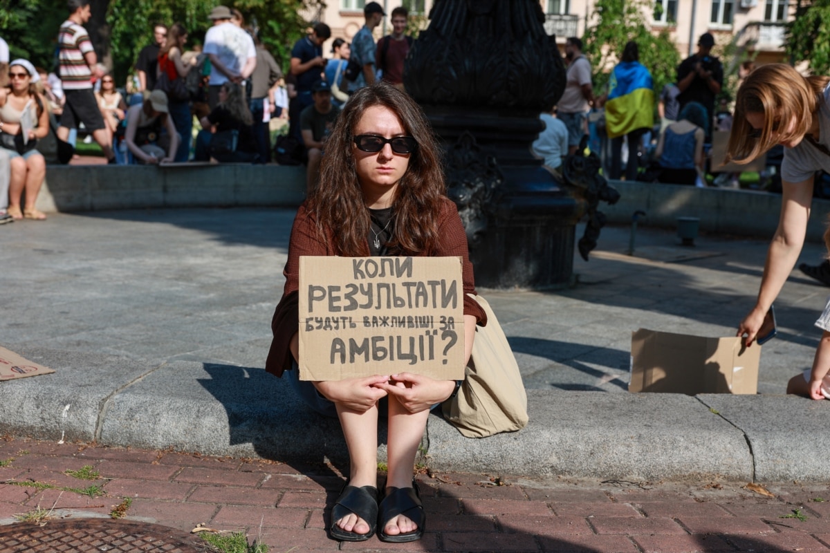 Дівчина прийшла на протест із запитанням на банері: «Коли результати будуть важливіші за амбіції?»