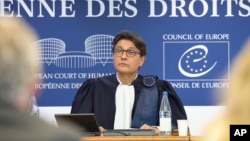 An image shows European Court of Human Rights (ECHR) President Mattias Guyomar reading the decisions before a packed courtroom in Strasbourg, France.
