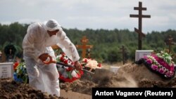 A grave digger wearing personal protective equipment as a preventive measure against COVID-19 buries a person at a graveyard on the outskirts of St. Petersburg on June 25.